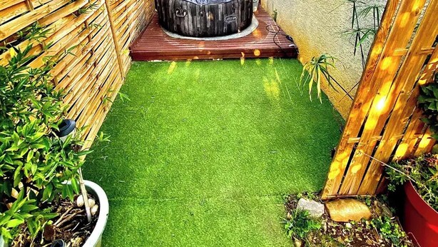 A small backyard with a hot tub, artificial grass, a wooden deck, and a wooden fence. - Loft ambrussum (Lunel)