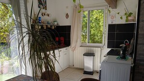 A kitchen with a window, a sink, a countertop with various items, and a dining table with a floral tablecloth. - Loft ambrussum (Lunel)
