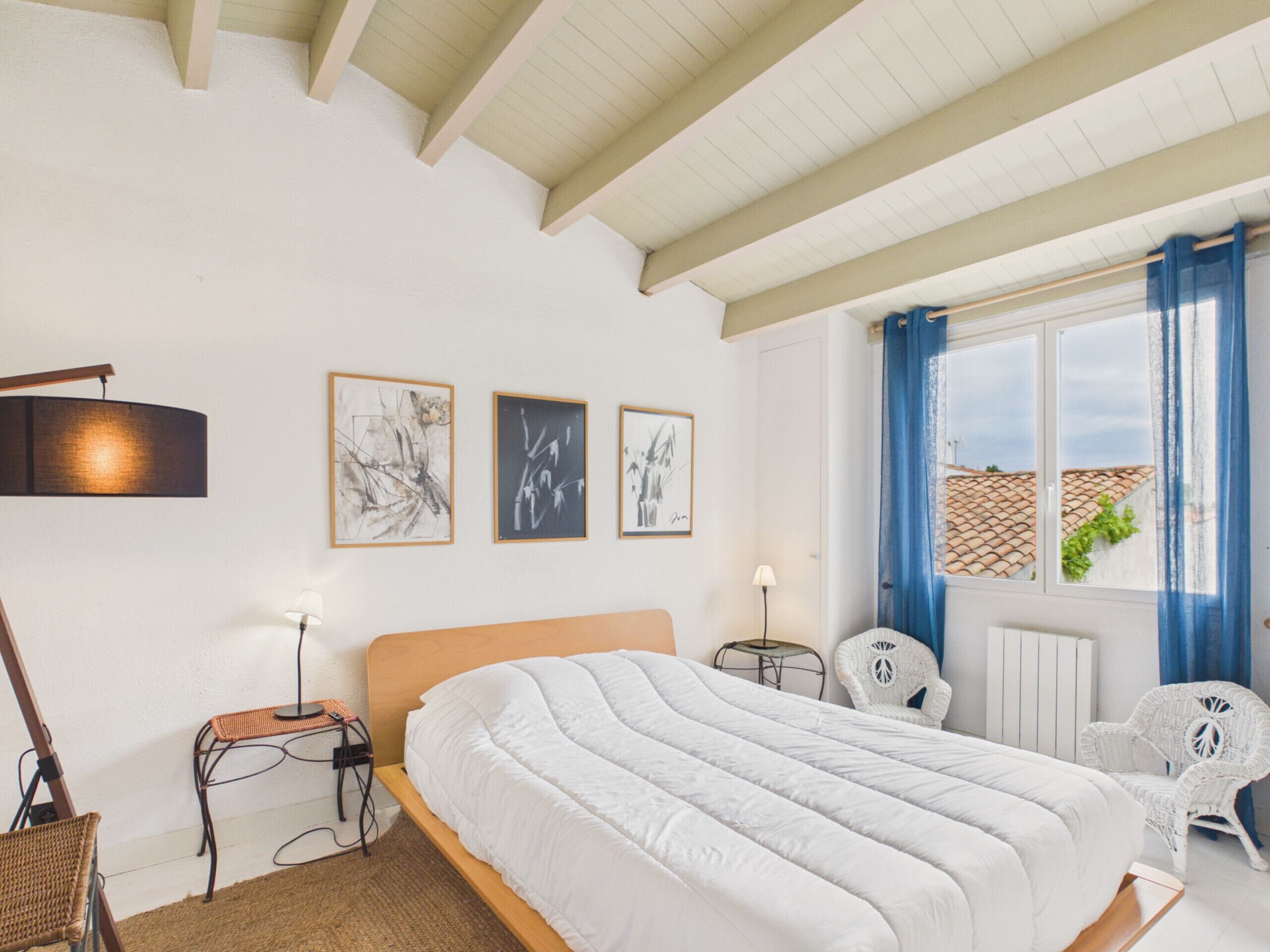 Een slaapkamer met een bed, een stoel, een tafel en drie ingelijste kunstwerken aan de muur.