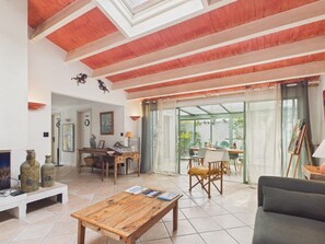 Ein geräumiger Wohnbereich mit Holzbalkendecke, einem Esstisch, einer Couch und Blick durch eine Glastür in einen Garten.