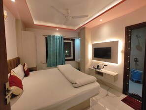 Une chambre à coucher avec un lit, un téléviseur fixé au mur, un ventilateur de plafond et une fenêtre avec des rideaux.