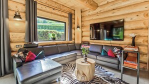 A cozy log cabin interior with a sectional sofa, a wooden coffee table, a zebra-patterned rug, and a TV mounted on the wall. - Vacation log cabin Schwarzwald 1 - Luxury chalet with sauna & whirlpool on the Feldberg (Feldberg (Schwarzwald))