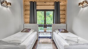 A room with two single beds, a wooden ceiling, a window with curtains, and a table with chairs outside. - Vacation log cabin Schwarzwald 1 - Luxury chalet with sauna & whirlpool on the Feldberg (Feldberg (Schwarzwald))