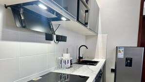 Una cocina moderna con una placa de inducción negra, un refrigerador de acero inoxidable y paredes de azulejos blancos.