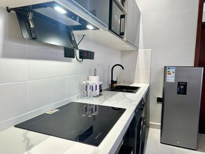 Eine moderne Küche mit einem schwarzen Induktionskochfeld, einem Edelstahlkühlschrank und weiß gefliesten Wänden.