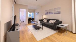 A modern living room with a sofa, coffee table, and TV stand. There is a dining area in the background with a table and chairs. - Bright one-bedroom flat with excellent amenities (Madrid)