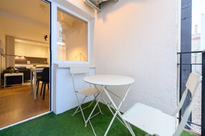 Ein kleiner, umzäunter Außenbereich mit einem weißen Tisch und Stühlen, einem Fenster und Blick in eine Küche.