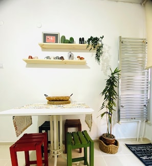 Una cocina con una mesa, taburetes, estantes con plantas y un radiador.