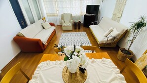 A living room with two sofas, a coffee table with a floral centerpiece, a television, and a potted plant. - Aydinoglu Suites (Denizli)