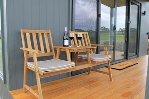 A wooden chair and table set on a wooden deck with a bottle of wine and two glasses. - Bellarine Villas 2 Bellarine Peninsula (Drysdale)