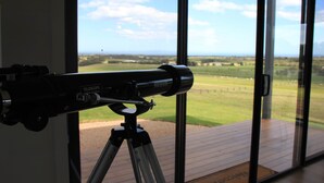 Un telescopio su un treppiede in una stanza con ampie finestre che si affacciano su un paesaggio erboso.