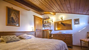 Una camera da letto con soffitto in legno, un letto con copriletto, un comò, uno specchio e una libreria.