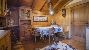 Una sala da pranzo in legno con un tavolo apparecchiato per quattro persone, sedie di legno, un tappeto in pelle di bovino, mobili contenitori in legno e un orologio a parete.