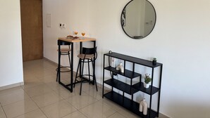 A small, clean room with a wooden table, two black chairs, a round mirror, and a black shelving unit with decorative items.