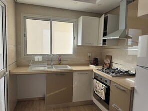 A modern kitchen with a double sink, stainless steel appliances, and a window providing natural light. - Bright apartment 5 minutes from the airport (Tunis)