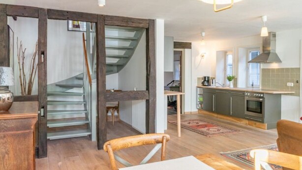 Une cuisine moderne dotée d’un four encastré, un coin repas avec une table et des chaises en bois, et un escalier menant à un autre niveau.