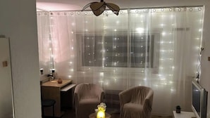 Una habitación acogedora con un escritorio, dos sillas, una mesita de noche con una lámpara y un televisor.