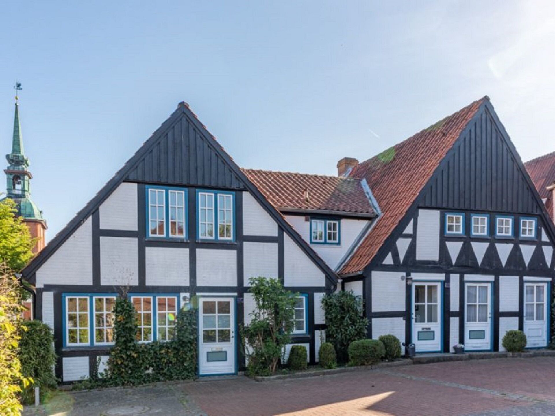 A traditional half-timbered house with a steeply pitched roof, white walls with black timber framing, and blue window frames.
