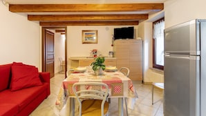 A dining area with a table set for four, a red sofa, and a kitchen with a refrigerator.
