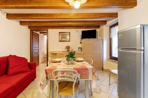 Zona pranzo con tavolo apparecchiato per quattro, un divano rosso e una cucina con frigorifero.