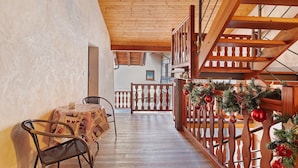 A wooden staircase with a railing decorated with Christmas ornaments, a table with chairs, and a view of a building in the background.