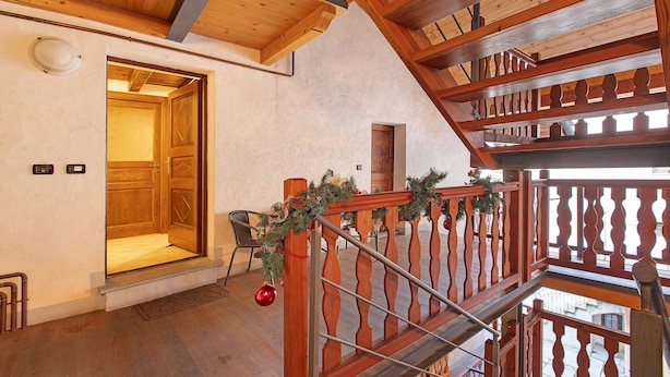 A wooden staircase with a railing, a door leading to a room, and a view of the outside.