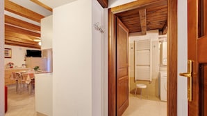 A room with a wooden ceiling, a white wall, a wooden door, a small stool, and a washing machine.