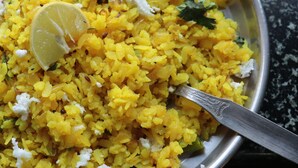 Un bol de riz jaune, garni de fromage blanc et d’une tranche de citron, est posé sur une assiette en métal.