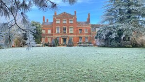 A large, red brick building with a symmetrical facade, multiple chimneys, and a central entrance. - The Potting Shed at Island Hall (Godmanchester)