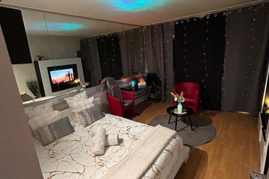 Une chambre d’hôtel moderne avec un grand lit, une télévision, un fauteuil rouge et une petite table sur laquelle est posé un vase.
