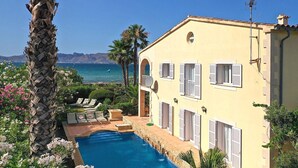 A yellow villa with a pool, outdoor seating, and a view of the sea. - Alcudia 1 | Seafront Barcares Villa | Frontline sea views and spacious 6-bed. (Pollensa)