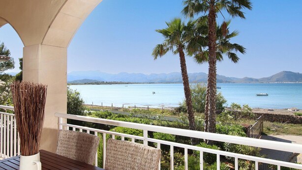 A balcony with a view of a calm sea, palm trees, and mountains in the distance. - Alcudia 1 | Seafront Barcares Villa | Frontline sea views and spacious 6-bed. (Pollensa)