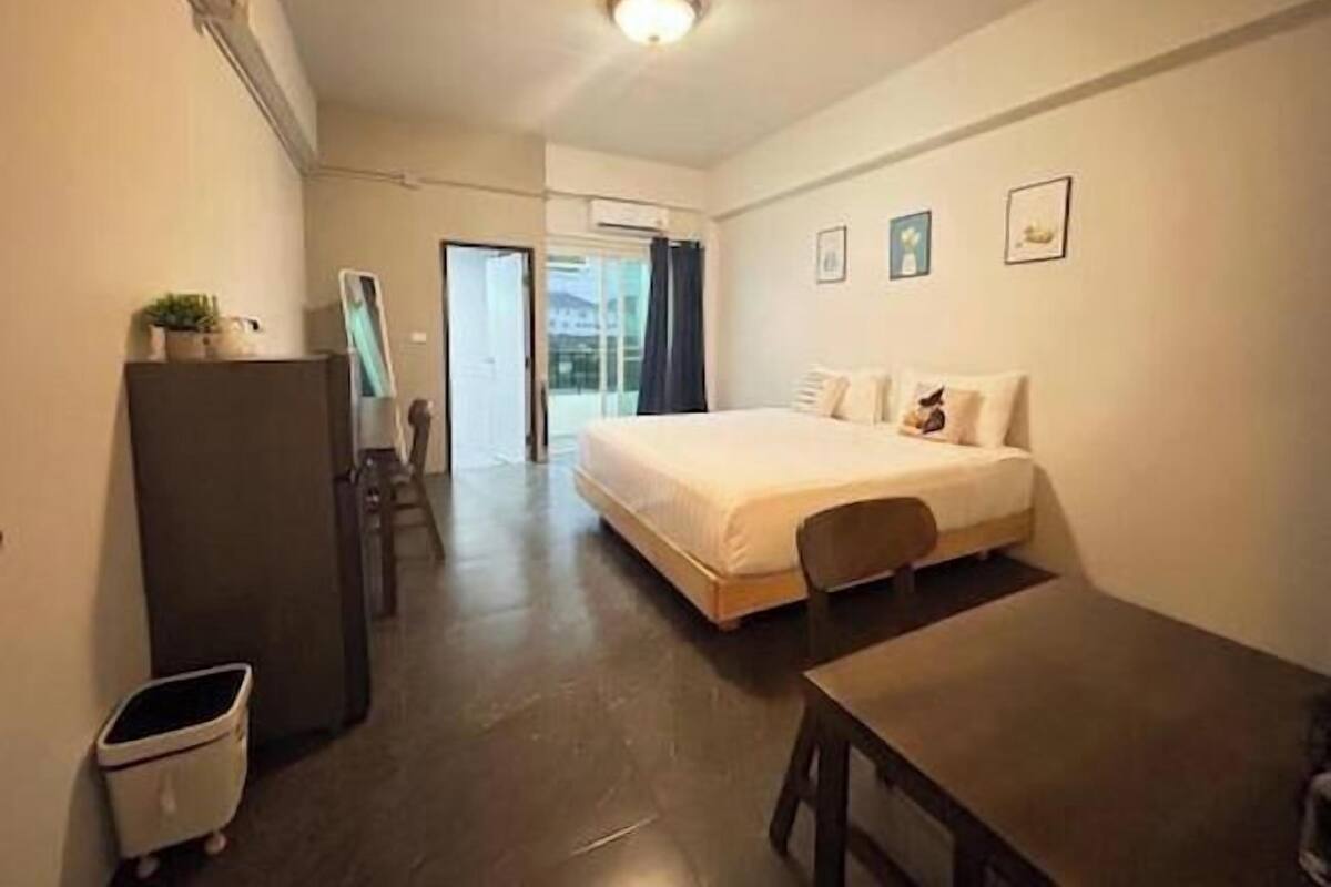 Quarto de hotel com cama, escrivaninha, cadeira, lixeira pequena e porta para uma varanda.