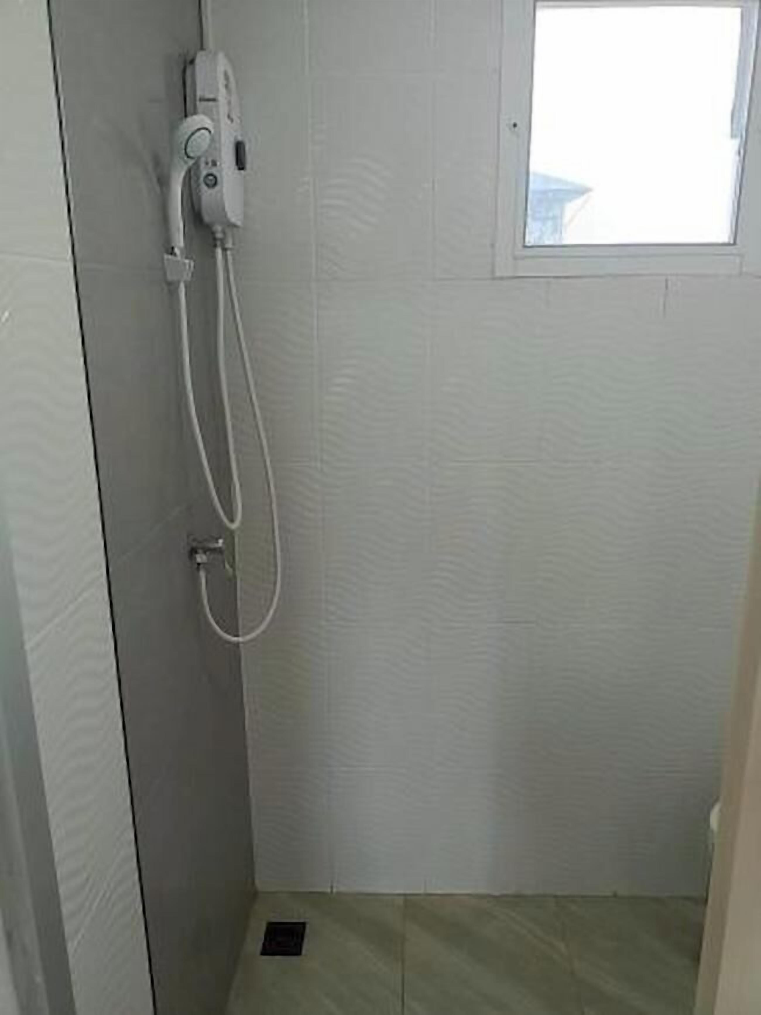 A small, enclosed shower area with a handheld showerhead, a control panel, and a window for natural light.