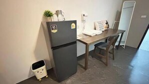 Pieni, käytännöllinen keittiönurkkaus, jossa on jääkaappi, pieni roskakori, puinen pöytä ja tuoli.