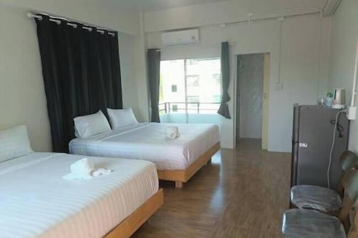 Quarto de hotel com duas camas, uma escrivaninha, uma cadeira e um frigorífico.