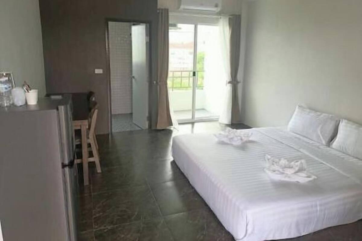 Quarto de hotel com cama, escrivaninha e cadeira. Possui uma varanda com vista para o exterior.