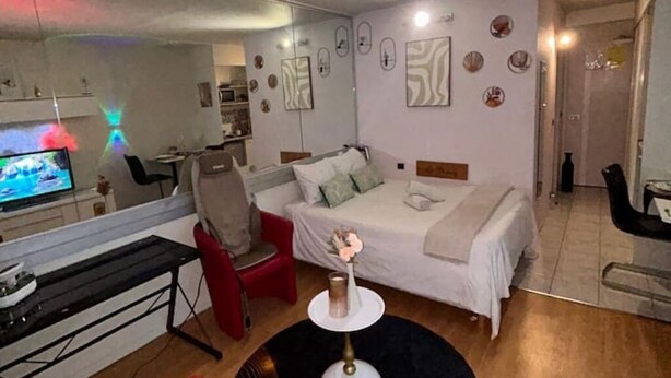 Ett kompakt hotellrum med en säng, ett litet skrivbord, en stol, en TV och en spegel.