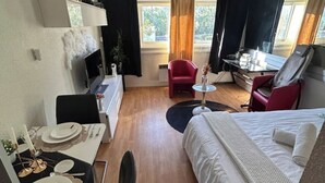 Ett hotellrum med en säng, ett skrivbord med en dator, en röd fåtölj, ett litet runt bord och en matplats med ett bord dukat för två personer.