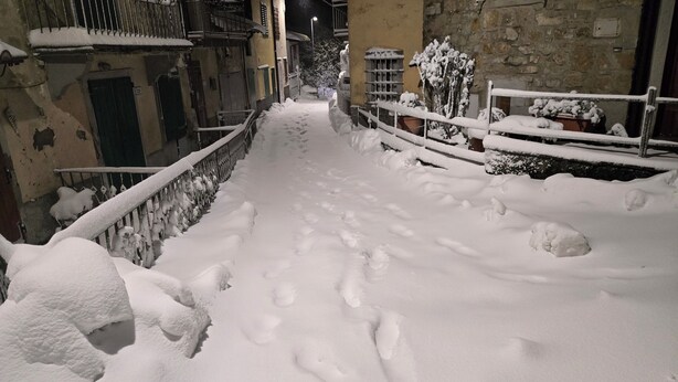 Une ruelle étroite, recouverte de neige, avec un mur de pierre d’un côté et une rambarde métallique de l’autre.
