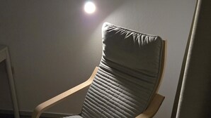 Un fauteuil moderne au design épuré, doté d’une structure en bois et d’un revêtement en tissu gris, placé dans une pièce au plancher en bois et au mur blanc.