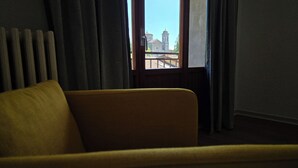 Une pièce avec un fauteuil jaune, une fenêtre avec des rideaux et une vue sur un immeuble doté de deux tours.