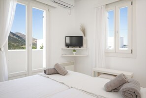 A hotel room with a bed, a TV on a shelf, a small table, and a view of the mountains. - Sunny villa with private pool and amazing views in Apollonia, Sifnos (Apollonia)