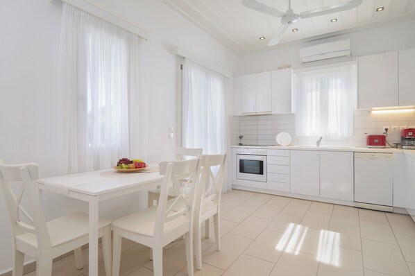 Une cuisine moderne avec des meubles blancs, une table à manger avec des chaises et un panier de fruits posé sur la table.