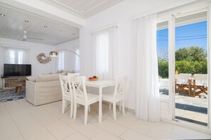 A modern living room with a sofa, dining table, and chairs, a flat-screen TV, and a balcony with outdoor seating.