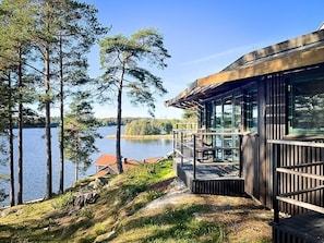 Een vakantiehuisje aan het meer met een houten terras en grote ramen met uitzicht op het water.