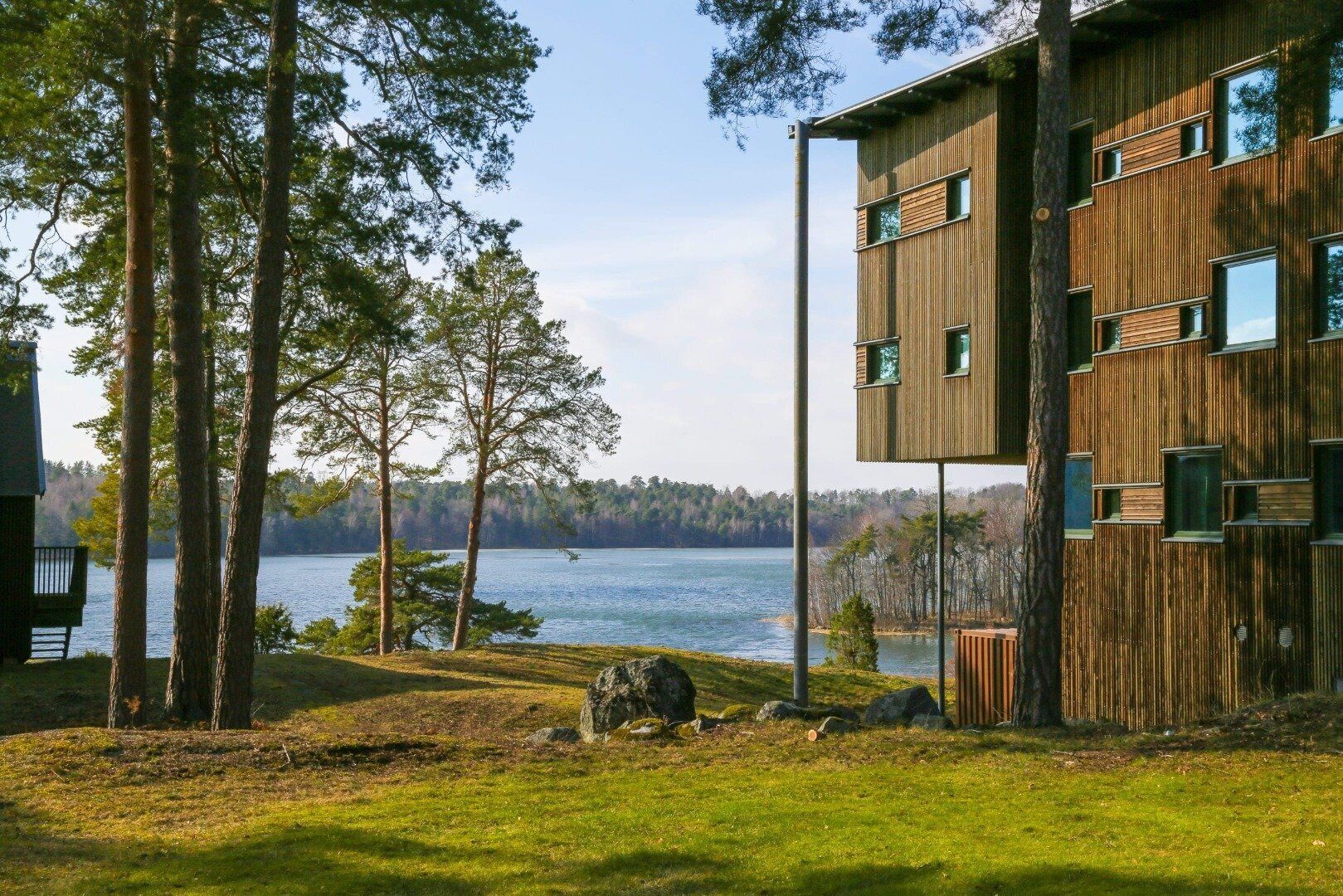 A modern building with a wooden facade, a view of a lake, and a forested area.