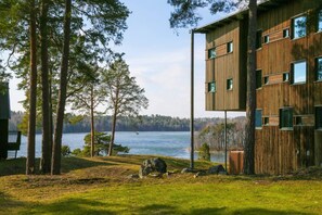 A modern building with a wooden facade, a view of a lake, and a forested area. - Sånga Hotell & Konferens  (Svartsjo)