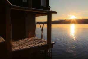 Een houten terras met een metalen hekwerk met uitzicht op een rustig wateroppervlak tijdens zonsondergang.