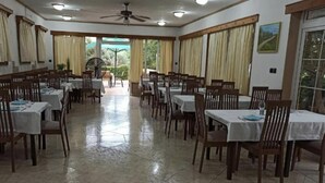 A dining area with tables and chairs, a ceiling fan, and large windows with curtains. - Tonino holiday house (Pag)